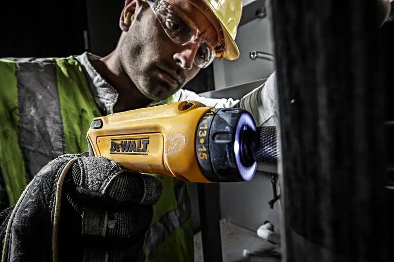 Photo of DEWALT DCF680G2 yellow electric screwdriver in use, worker in safety gear holding tool.