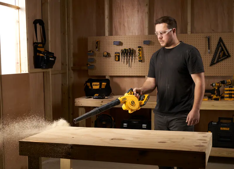 Photo of man using DEWALT blower DCV100, DCV100-XJ cleaning wood dust in workshop.