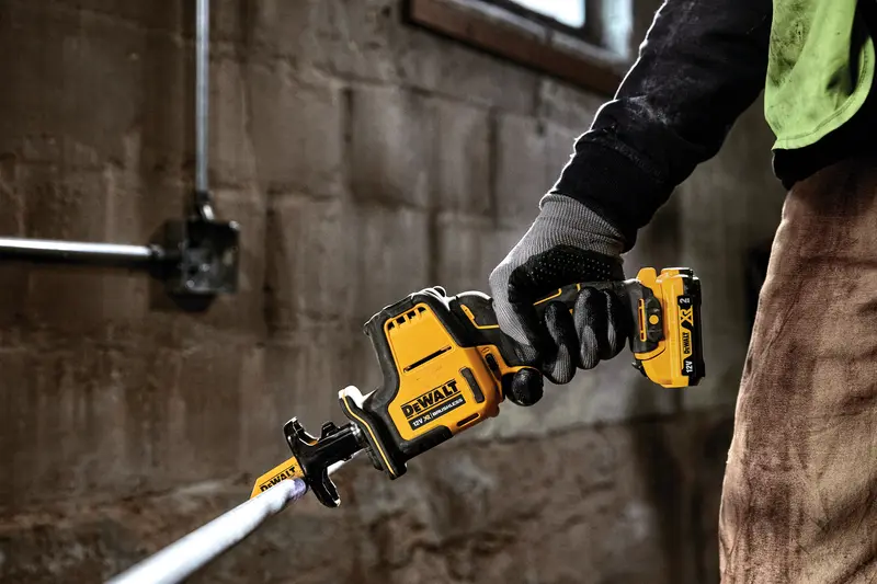 Photo of DEWALT DCS312D2 cordless reciprocating saw in use cutting pipe, close-up view.